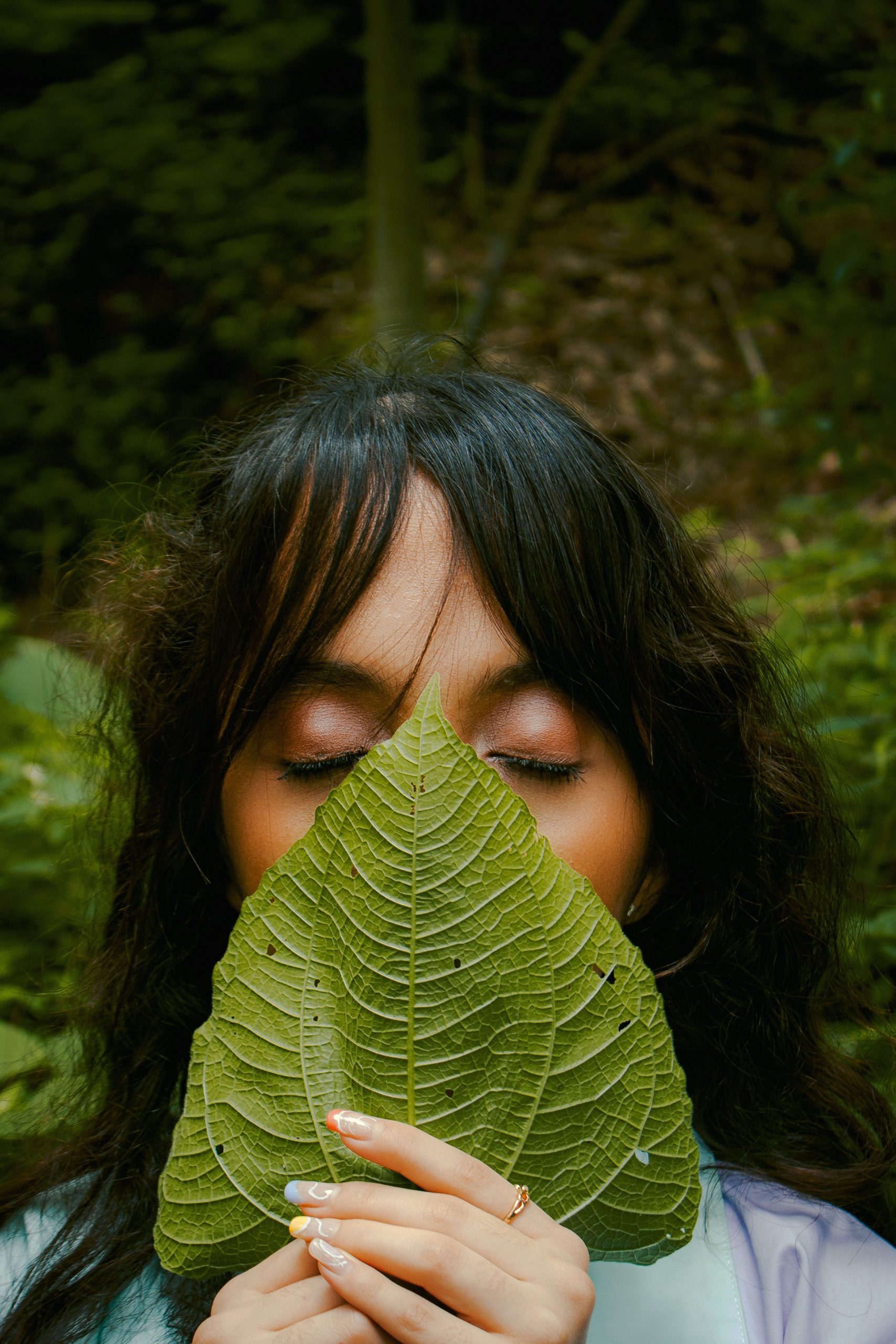 Woman posing with eyes closed, holding a large green leaf for artistic effect.